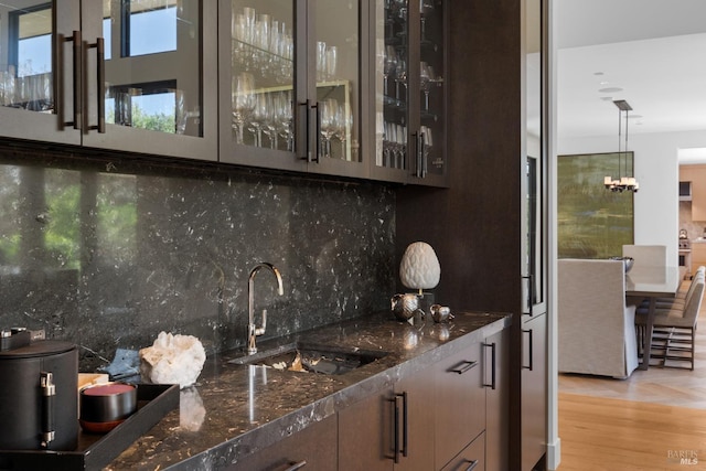 bar featuring light wood-style flooring, a sink, wet bar, an inviting chandelier, and decorative backsplash