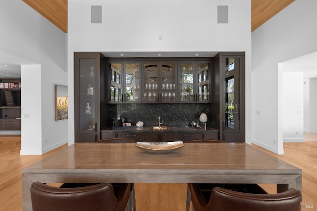bar featuring a towering ceiling, wet bar, a sink, baseboards, and light wood-style flooring