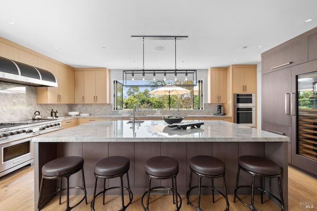 kitchen with ventilation hood, luxury stove, light brown cabinets, a sink, and tasteful backsplash