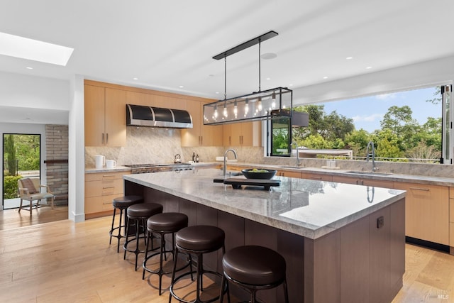 kitchen with light brown cabinets, wall chimney range hood, modern cabinets, and a sink