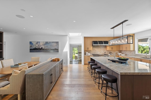 kitchen featuring range hood, a large island, a sink, decorative backsplash, and a kitchen bar