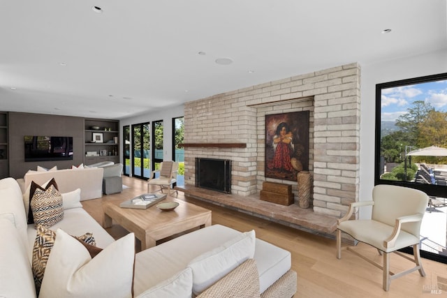 living room featuring wood finished floors, a brick fireplace, and built in shelves
