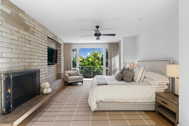 bedroom featuring a brick fireplace, wood finished floors, and a ceiling fan
