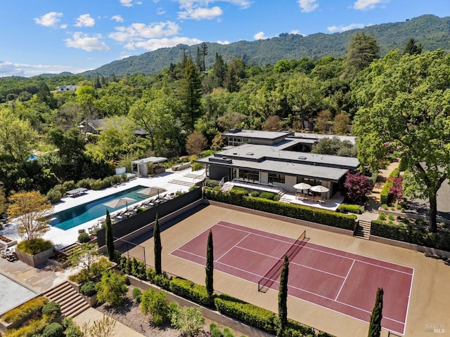 view of sport court featuring fence, an outdoor pool, a view of trees, and a mountain view
