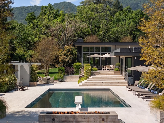 outdoor pool featuring a patio area, a diving board, a view of trees, a mountain view, and stairs