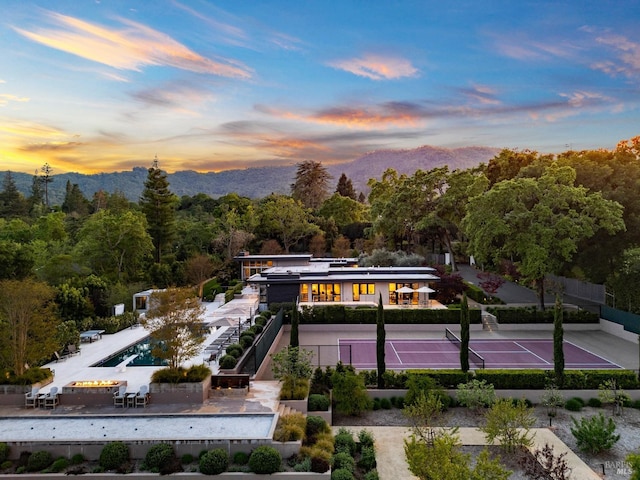 exterior space with fence, a view of trees, a tennis court, and a mountain view