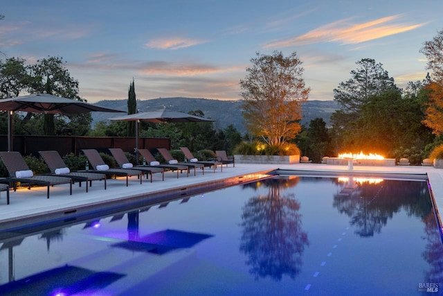 pool at dusk with a mountain view, an outdoor fire pit, a patio, and a fenced in pool