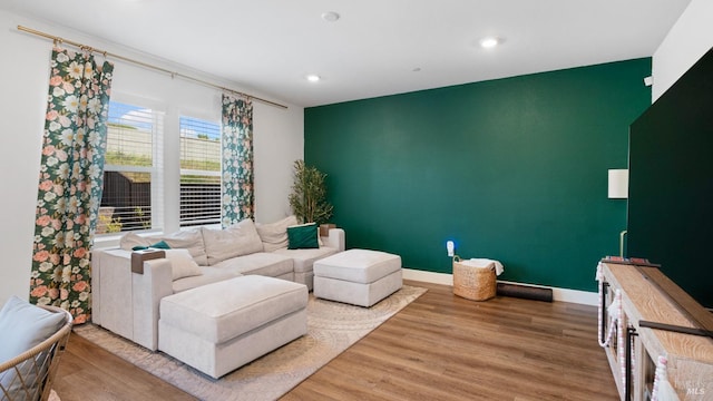 living room featuring light wood finished floors, an accent wall, baseboards, and recessed lighting