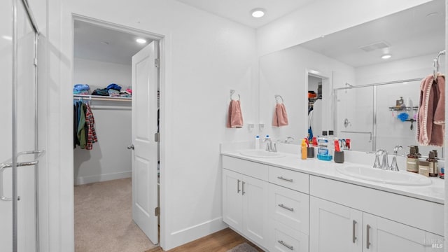 bathroom featuring baseboards, a sink, a shower stall, and double vanity