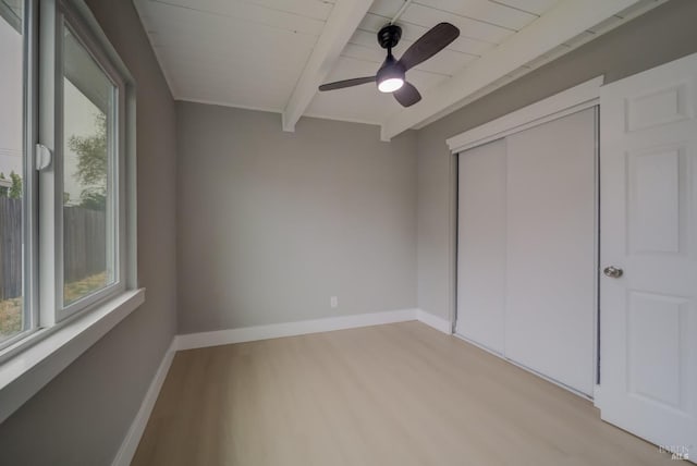 unfurnished bedroom featuring a closet, light wood-style flooring, beam ceiling, and multiple windows