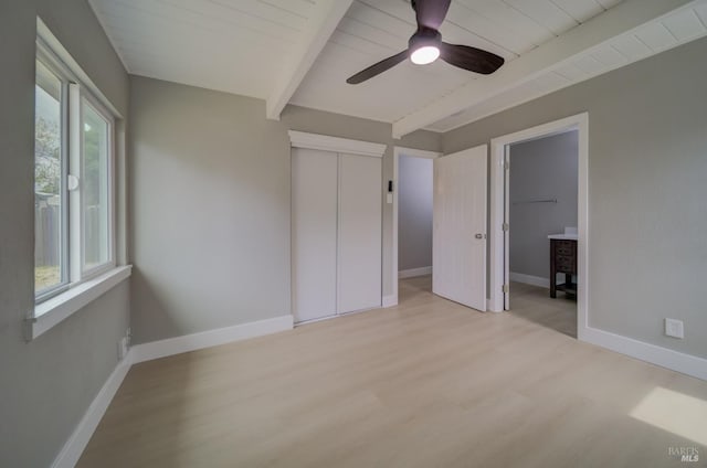 unfurnished bedroom featuring beamed ceiling, baseboards, and light wood finished floors
