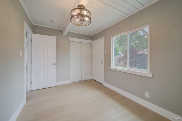 unfurnished bedroom with baseboards, light wood finished floors, beam ceiling, and a chandelier