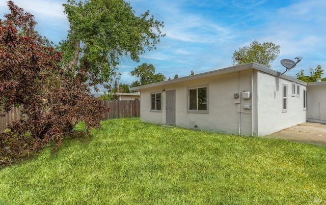 back of house featuring a lawn, stucco siding, and fence
