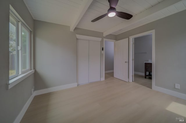 unfurnished bedroom featuring baseboards, beam ceiling, light wood-style flooring, and a closet