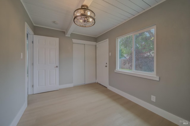 unfurnished bedroom featuring an inviting chandelier, baseboards, light wood-type flooring, beamed ceiling, and a closet