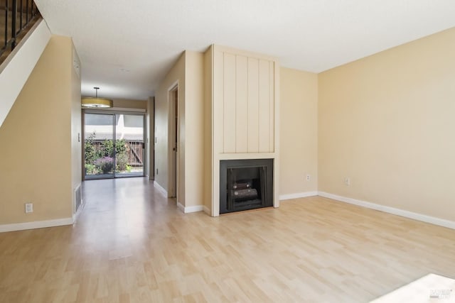 unfurnished living room featuring light wood-style flooring, visible vents, baseboards, a large fireplace, and stairs