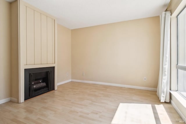 unfurnished living room featuring baseboards, a large fireplace, and light wood-style flooring