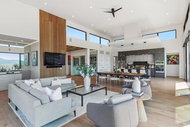 living area with a ceiling fan, a high ceiling, plenty of natural light, and light wood-type flooring