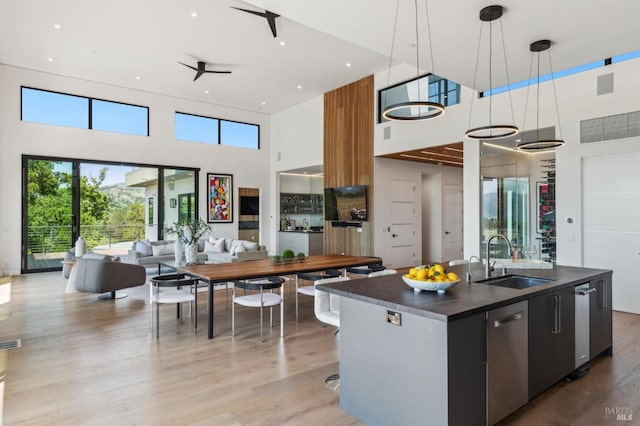 kitchen featuring a towering ceiling, dark countertops, stainless steel dishwasher, a sink, and open floor plan