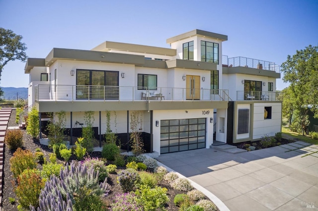view of front of property featuring concrete driveway, an attached garage, a balcony, and stucco siding