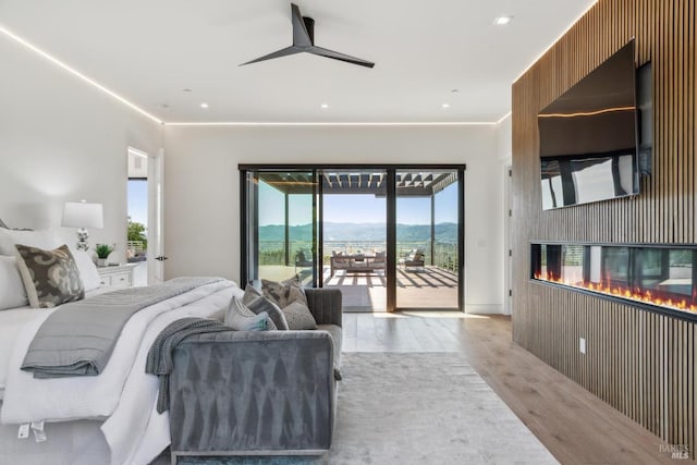 bedroom with light wood-style floors, recessed lighting, a multi sided fireplace, and access to exterior