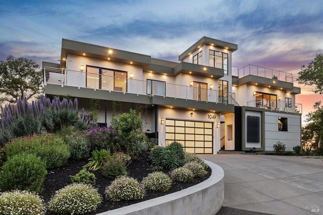 contemporary house with an attached garage, stucco siding, a balcony, and concrete driveway