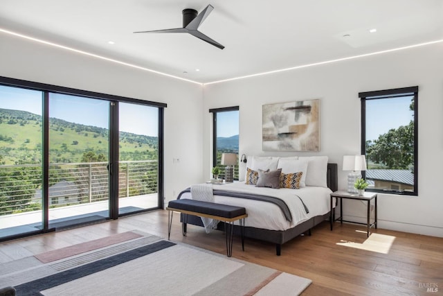 bedroom featuring access to outside, ceiling fan, a mountain view, and wood finished floors