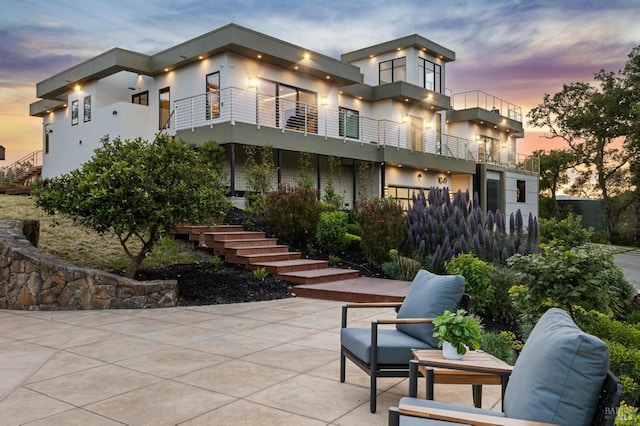 rear view of property featuring a patio, stucco siding, stairway, and a balcony