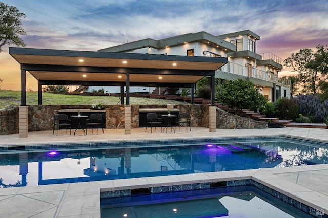 pool at dusk with stairway, an in ground hot tub, an outdoor pool, and outdoor dry bar