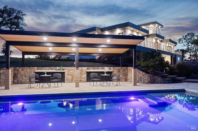 pool at dusk with a patio and an outdoor pool
