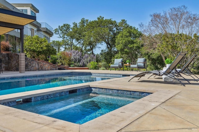 outdoor pool with an in ground hot tub and a patio area