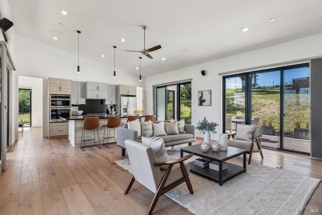living area featuring light wood-style floors, high vaulted ceiling, a ceiling fan, and a healthy amount of sunlight