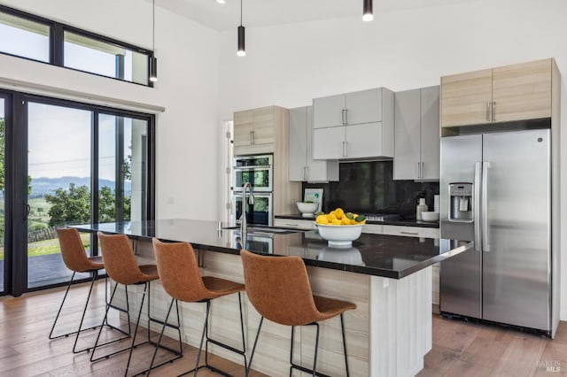 kitchen with dark countertops, an island with sink, tasteful backsplash, a sink, and appliances with stainless steel finishes
