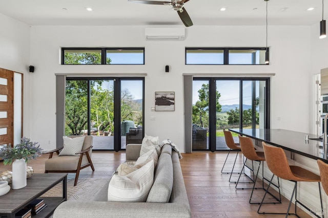 living area with an AC wall unit, a high ceiling, a wealth of natural light, and light wood-style floors