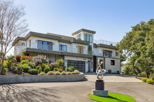 view of front facade with an attached garage, stucco siding, a balcony, and concrete driveway