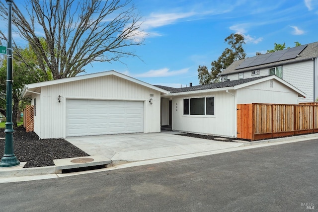 view of front of home featuring an attached garage, driveway, fence, and roof mounted solar panels