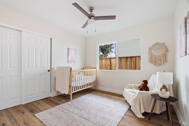 bedroom featuring baseboards, a ceiling fan, wood finished floors, a closet, and a nursery area