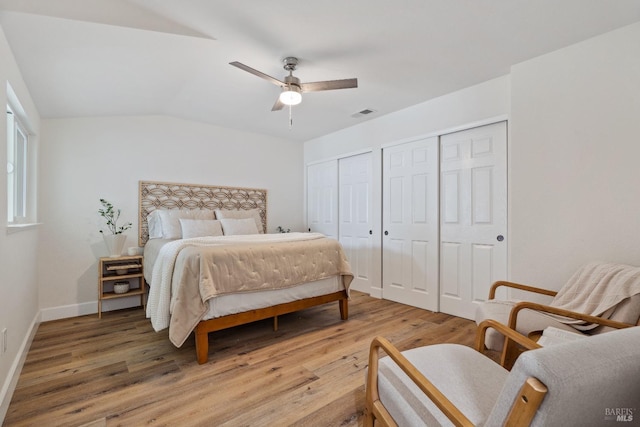 bedroom with light wood-type flooring, two closets, baseboards, lofted ceiling, and visible vents
