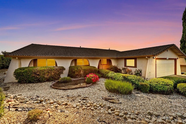 ranch-style house featuring an attached garage, a tiled roof, and stucco siding