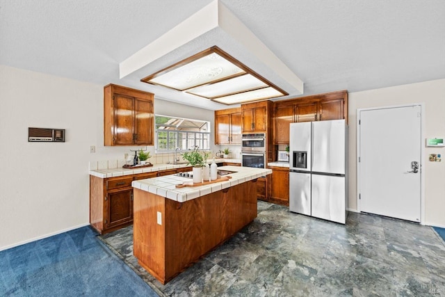 kitchen featuring tile countertops, brown cabinetry, stainless steel appliances, and a sink