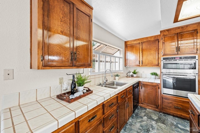 kitchen featuring tile counters, a sink, brown cabinets, double oven, and black dishwasher