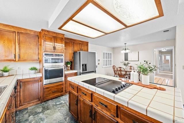 kitchen featuring tile countertops, brown cabinetry, stainless steel appliances, and visible vents