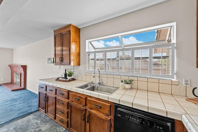 kitchen with a sink, brown cabinetry, tile countertops, a brick fireplace, and black dishwasher
