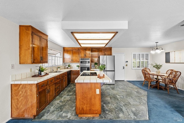 kitchen with tile counters, stainless steel appliances, a sink, a center island, and a chandelier