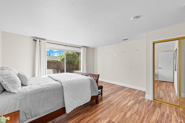 bedroom with a textured ceiling, wood finished floors, visible vents, and baseboards