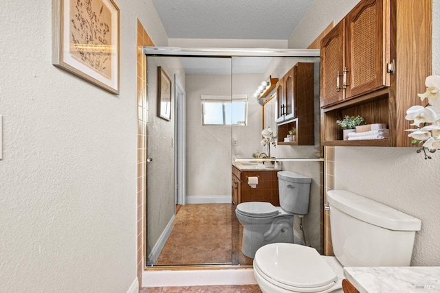 bathroom featuring a shower stall, toilet, vanity, baseboards, and a textured ceiling
