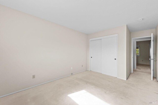 unfurnished bedroom featuring light carpet, a closet, and baseboards