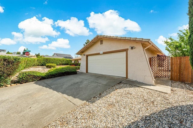 view of side of home featuring stucco siding, an attached garage, concrete driveway, and fence