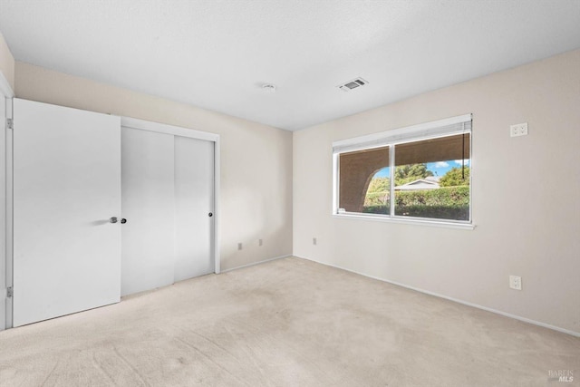 unfurnished bedroom featuring light colored carpet, baseboards, visible vents, and a closet