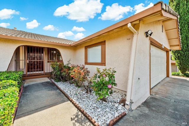 doorway to property featuring a garage, concrete driveway, and stucco siding
